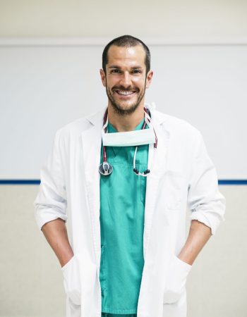 Smiling handsome doctor at hospital. Standing. Looking at camera.