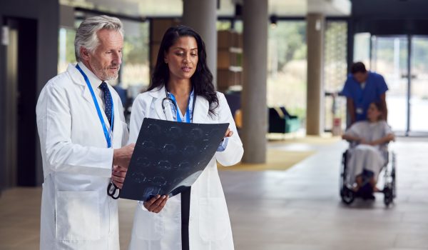 Two Doctors In White Coats And Discussing Patient Scan In Busy Hospital